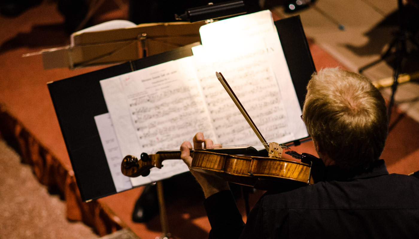 Man spielt Geige und liest Noten auf beleuchtetem Notenständer