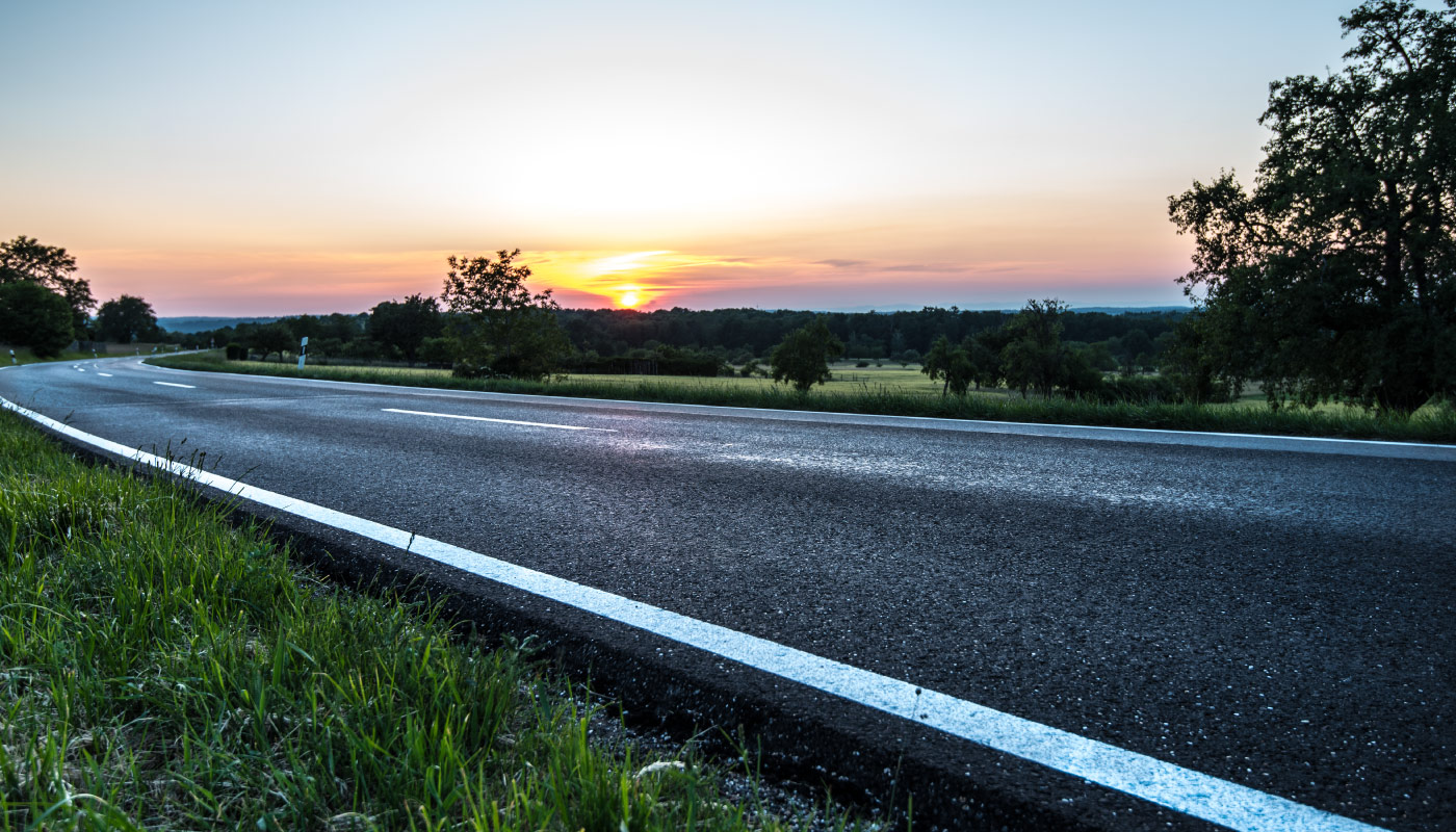 Straße im Sonnenuntergang mit Bäumen und farbigem Himmel