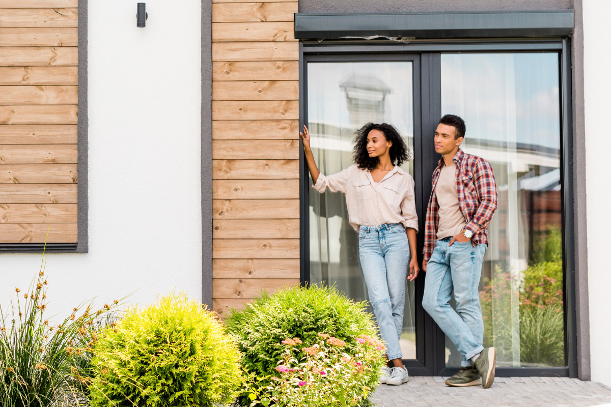 Zwei Personen vor modernem Gebäude mit Holzverkleidung und Garten.