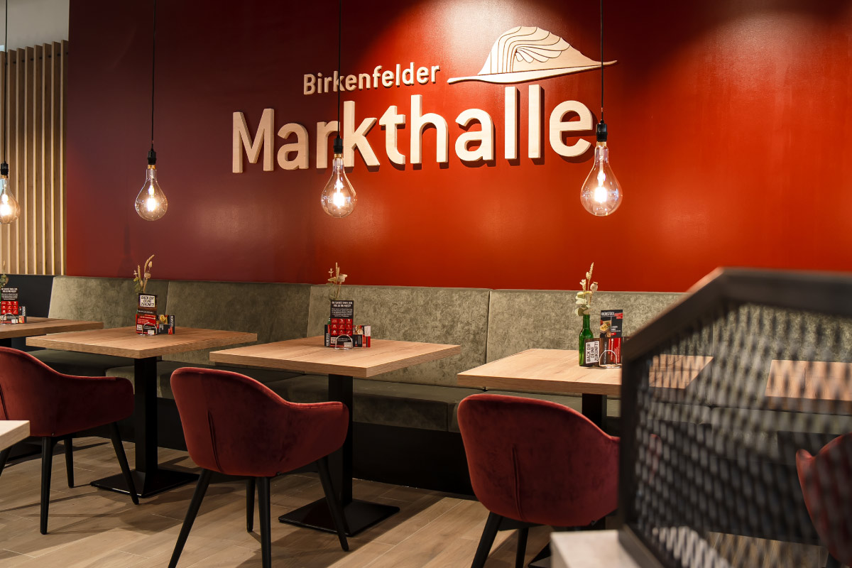 Innenraum der Birkenfelder Markthalle mit roten Samtstühlen, Hängelampen und dekorierten Tischen
